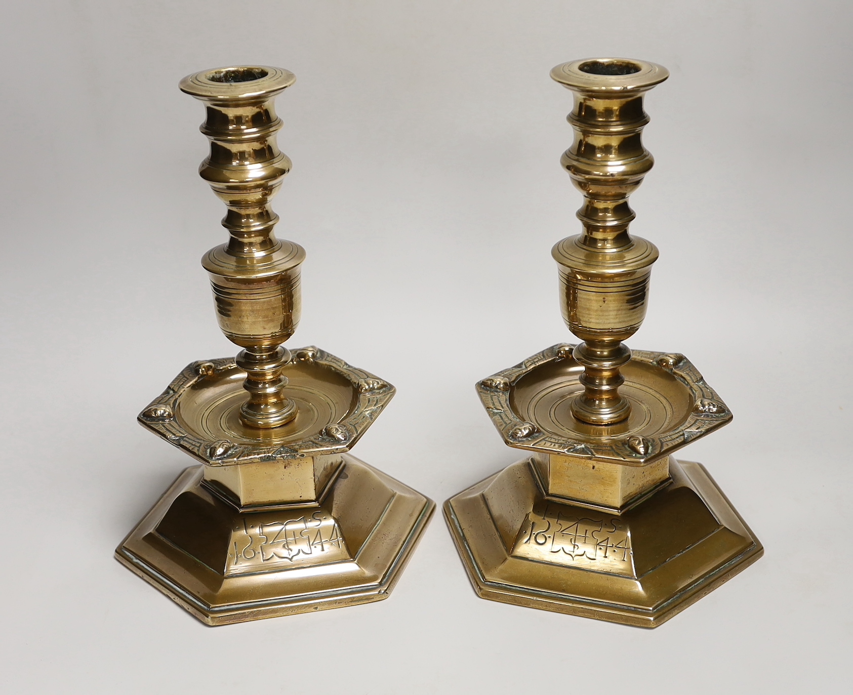 A pair of Scandinavian, possibly 17th century, brass candlesticks, dated 1644, each with a shield enclosing merchants mark, each with hexagonal base and hexagonal drip tray cast with marks, 27cm